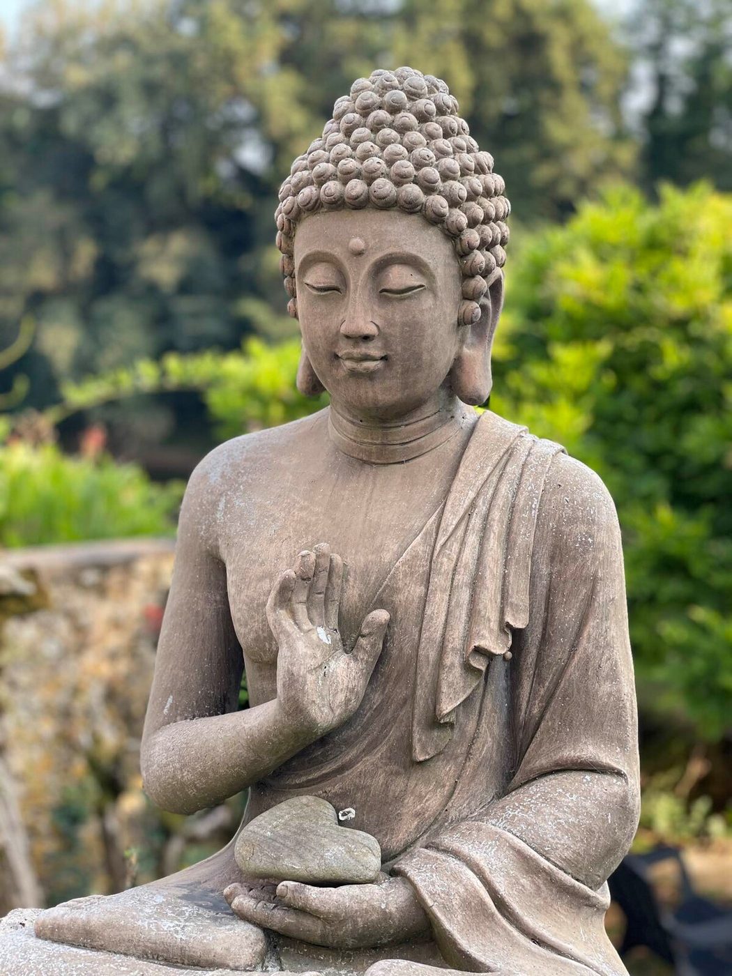 Statue de Bouddha tenant un galet en forme de cœur, dans le jardin