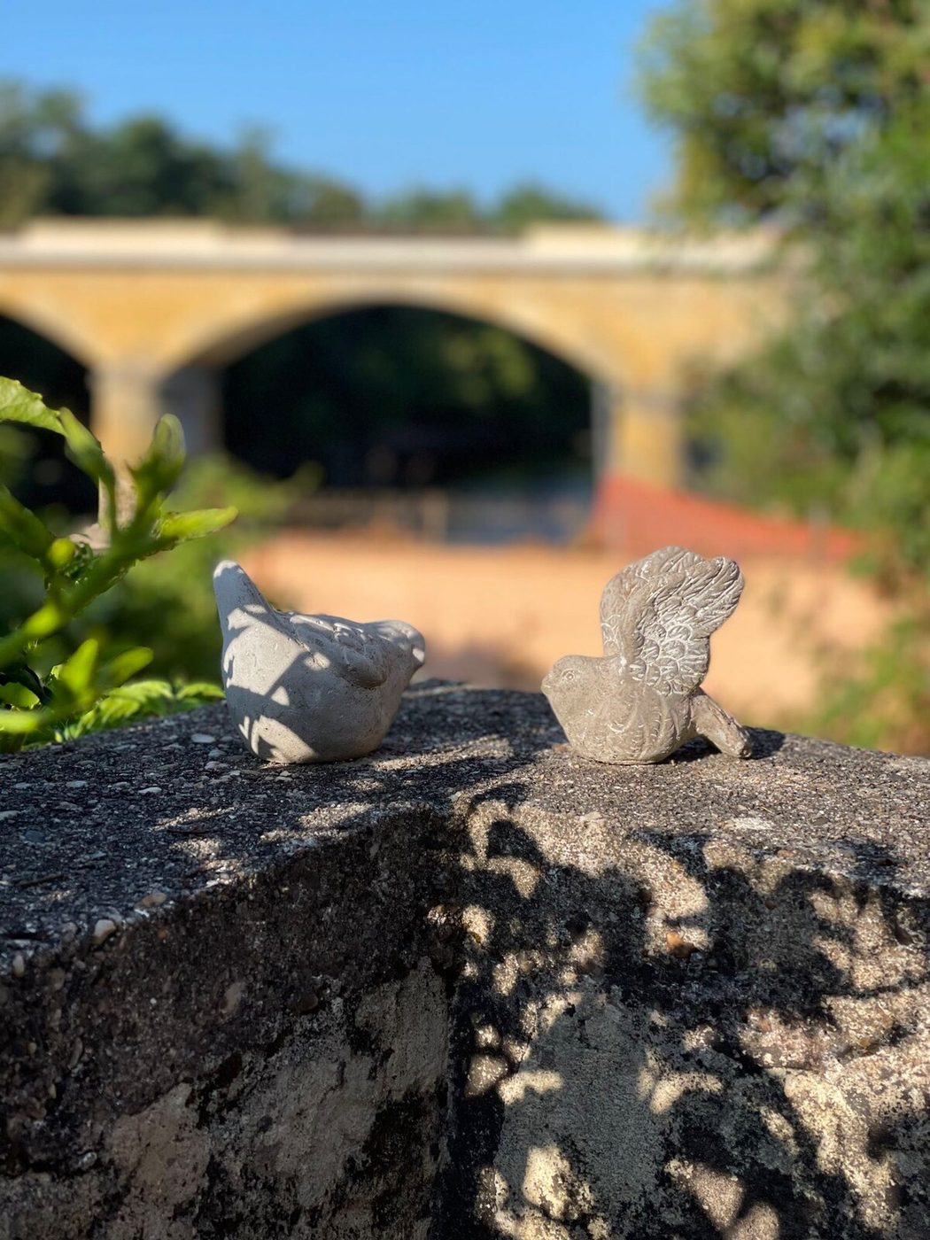 Deux oiseaux en pierre posés sur un muret, pont de pierre en arrière-plan